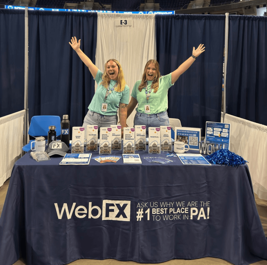 Julie e Emily estão em frente a uma mesa do Webfx em uma feira de carreira