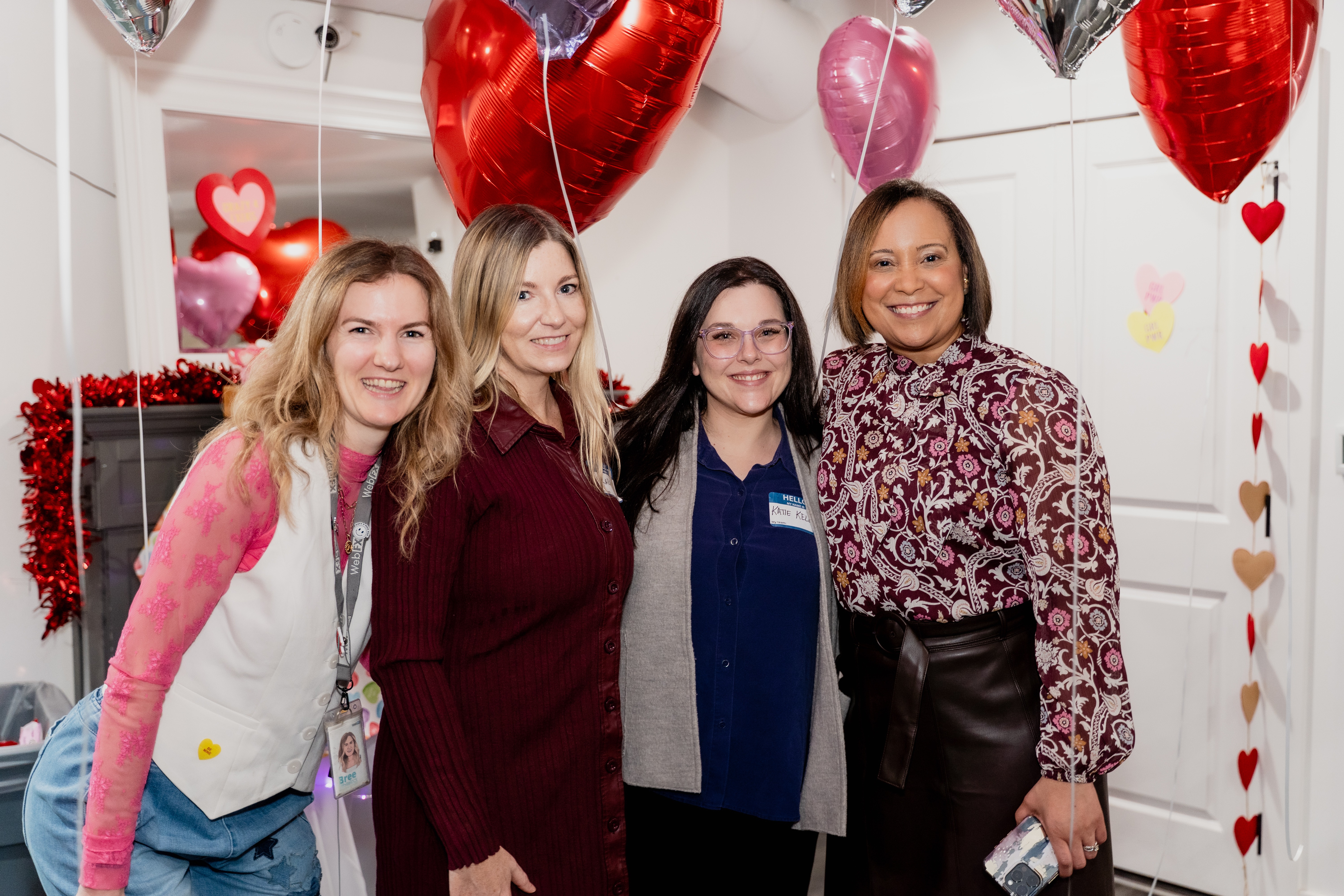 Quatro mulheres posando para uma foto com balões de coração ao fundo