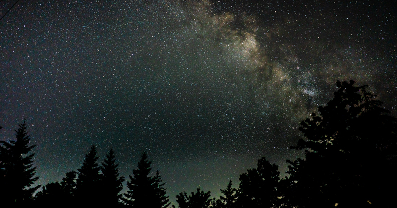 Visão do céu noturno cheio de estrelas e com prédios ao fundo